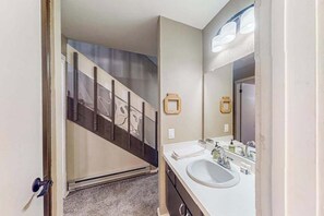 A bathroom with a white sink, a mirror, and a staircase leading to another room.