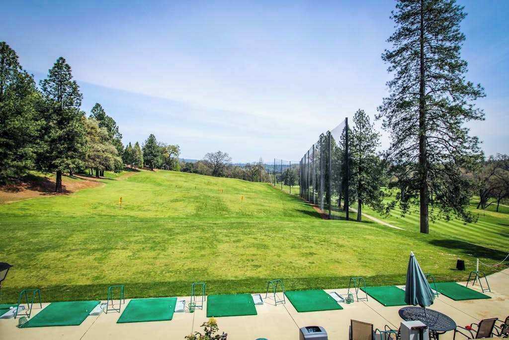 A golf course with a clear view of the fairway, a putting green, and a clubhouse area with seating and a table.