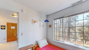 A bedroom with a single bed, a window with a view of trees, a bedside table, and a door leading to another room. - Escape to Yosemite - Pine Mountain Lake (Groveland)