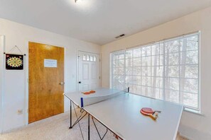 Una habitación con mesa de ping pong, una puerta y una ventana con persianas.