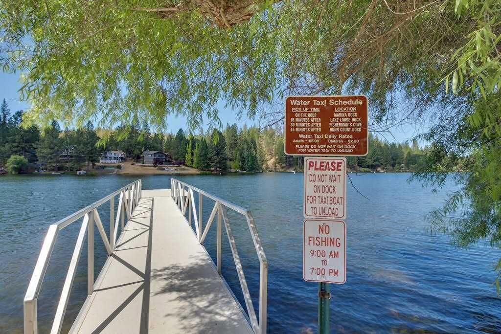 Un muelle que conduce a una masa de agua, con un letrero que indica el horario de un taxi acuático y un letrero de 'no se permite la pesca'.