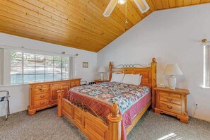 Un dormitorio con techo de madera, una cama con colcha, dos mesitas de noche con lámparas y una ventana.