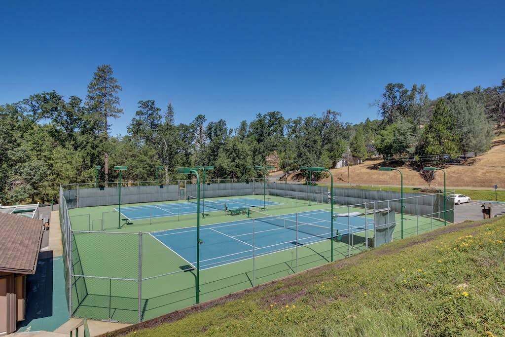 An outdoor tennis court with a net, surrounded by a fence, and trees in the background.