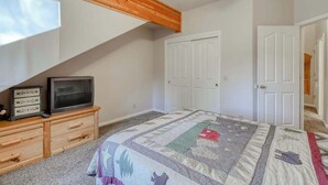 Ein Schlafzimmer mit einem Bett, einem Fernseher auf einer Holzkommode, einer Steppdecke und weißen Türen.