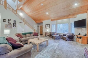 A spacious living room with a high ceiling, a staircase, and a television mounted on the wall. - Hatcher's Hideaway - Ockenden Ranch (Shaver Lake)