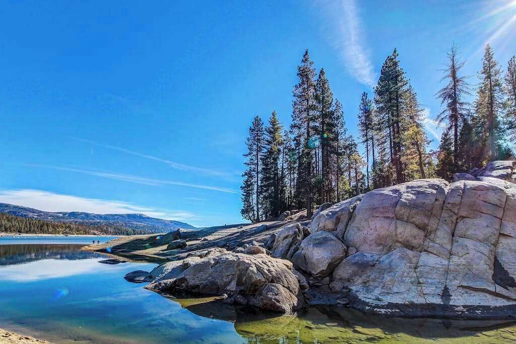 A natural landscape with a large rock formation, a calm lake, and a forest of tall trees.