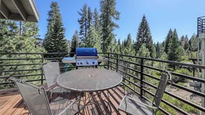 An outdoor deck with a grill, seating, and a view of tall trees. - Eagle's Rest - Huntington Lake (Lakeshore)