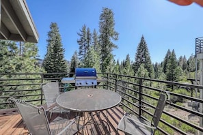 Terraza al aire libre con una parrilla, asientos y vistas a árboles altos.