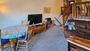 A living room with a dining table, chairs, a sofa, a TV, and a bookshelf. - Huntington Hideaway - Huntington Lake (Lakeshore)