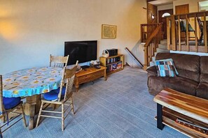 A living room with a dining table, chairs, a sofa, a TV, and a bookshelf. - Huntington Hideaway - Huntington Lake (Lakeshore)