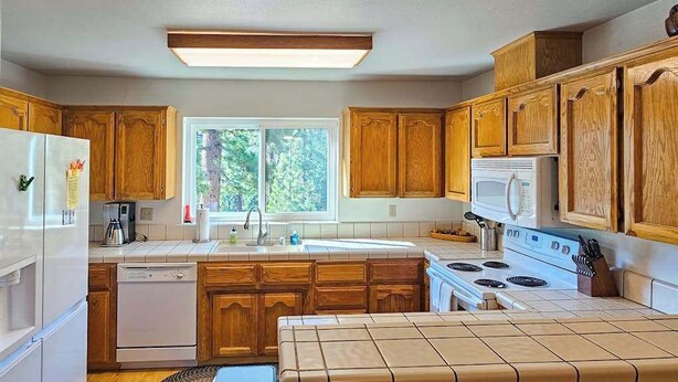 A kitchen with wooden cabinets, a white refrigerator, a dishwasher, a stove, and a window providing natural light. - Huntington Hideaway - Huntington Lake (Lakeshore)
