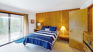 A bedroom with a bed, two bedside tables, a wooden wardrobe, a sliding glass door to a balcony, and a view of trees. - Huntington Hideaway - Huntington Lake (Lakeshore)