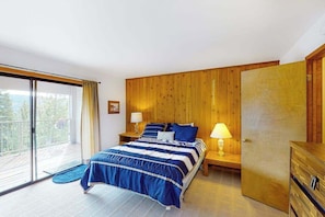 A bedroom with a bed, two bedside tables, a wooden wardrobe, a sliding glass door to a balcony, and a view of trees. - Huntington Hideaway - Huntington Lake (Lakeshore)