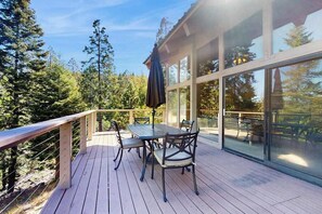 Eine Holzterrasse mit Tisch und Stühlen, umgeben von Glaswänden und Blick auf Bäume.