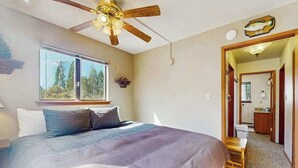 Una camera da letto con un letto, una ventola a soffitto, una finestra e un ingresso che porta al bagno.