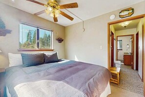 Ein Schlafzimmer mit Bett, Deckenventilator, Fenster und einer Tür zu einem Badezimmer.