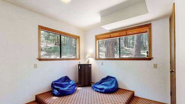 A room with two beds, a small cabinet, and two windows with a forest view. - Cresta Cabin - Pinebrook (Arnold)