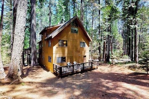 A wooden cabin with a porch and a fenced deck, surrounded by tall trees. - Cresta Cabin - Pinebrook (Arnold)