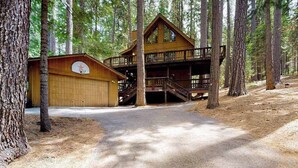 A cabin with a two-story deck, a garage, and a dirt path surrounded by trees. - Cresta Cabin - Pinebrook (Arnold)