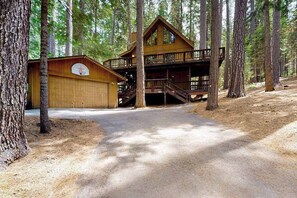 A cabin with a two-story deck, a garage, and a dirt path surrounded by trees. - Cresta Cabin - Pinebrook (Arnold)