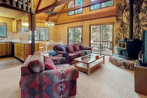 A spacious living area with a fireplace, a dining area, and a kitchen. - Cresta Cabin - Pinebrook (Arnold)