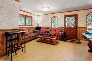 A cozy living room with a pool table, a striped sofa, a brown couch, and a wooden bar area. - Cresta Cabin - Pinebrook (Arnold)