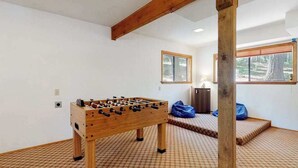 A room with a wooden foosball table, checkered carpet, and a window with a view of trees. - Cresta Cabin - Pinebrook (Arnold)