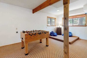 A room with a wooden foosball table, checkered carpet, and a window with a view of trees. - Cresta Cabin - Pinebrook (Arnold)