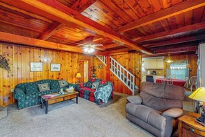 L’intérieur d’un chalet accueillant, avec un plafond en bois, un canapé, un fauteuil, une table à manger et un escalier.