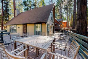 A wooden cabin with a deck, surrounded by tall trees. - Casita Villareal - East Village (Shaver Lake)