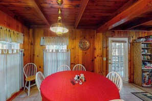 A wooden interior with a round table, white chairs, a chandelier, and a bookshelf. - Casita Villareal - East Village (Shaver Lake)