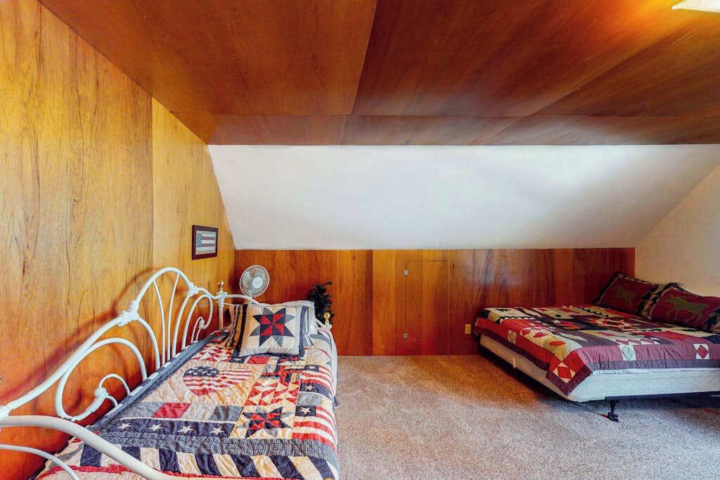 Un dormitorio con dos camas, paneles de madera en las paredes y techo inclinado.