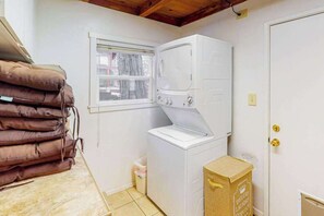 A laundry room with a washing machine, a window, a door, and a stack of brown cushions. - Casita Villareal - East Village (Shaver Lake)
