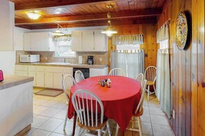 Une cuisine avec des meubles blancs, un four à micro-ondes et une machine à café. On y trouve une table à manger recouverte d’une nappe rouge et entourée de chaises blanches.