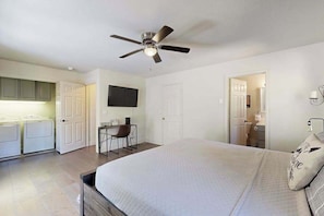 A bedroom with a bed, a desk, and a chair. There is a ceiling fan, a television, and a door leading to a bathroom. - Pine Mountain Retreat (Groveland)