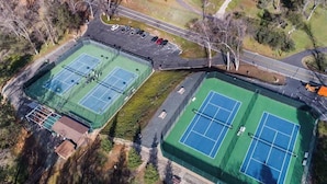 Eine Vogelperspektive eines Tennisplatzkomplexes mit mehreren Plätzen, einem Parkplatz und umliegender Bepflanzung.