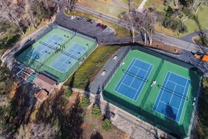 Eine Vogelperspektive eines Tennisplatzkomplexes mit mehreren Plätzen, einem Parkplatz und umliegender Bepflanzung.