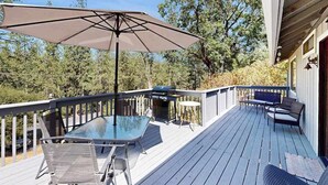Eine Terrasse mit Glastisch, Stühlen, einem Grill und einem großen Sonnenschirm.