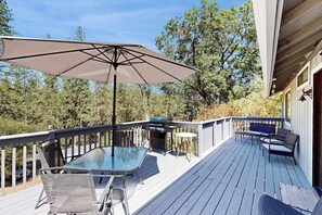Eine Terrasse mit Glastisch, Stühlen, einem Grill und einem großen Sonnenschirm.