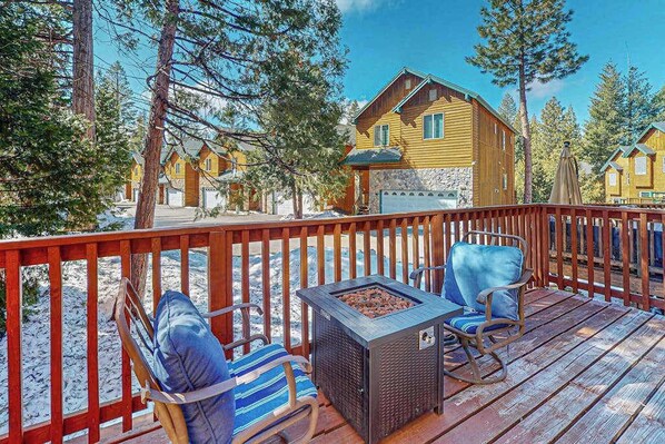 A wooden deck with two chairs and a fire pit, overlooking a cabin with a stone facade. - It's Cabin Time - Sierra Pines (Shaver Lake)