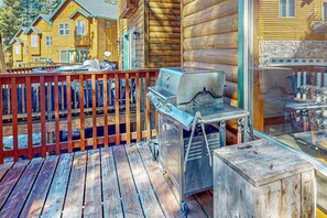 Eine Holzdielen-Terrasse mit einem Grill, einem Holzzaun und Blick auf ein gelbes Gebäude.