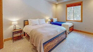 Una camera da letto con un letto grande, un letto più piccolo, un comodino con una lampada e una finestra vista alberi.