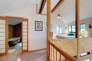 Ein Zimmer mit Holzboden, einem Bett mit Kissen, einem Nachttisch, einem Fenster und einem Badezimmer mit einer Badewanne.