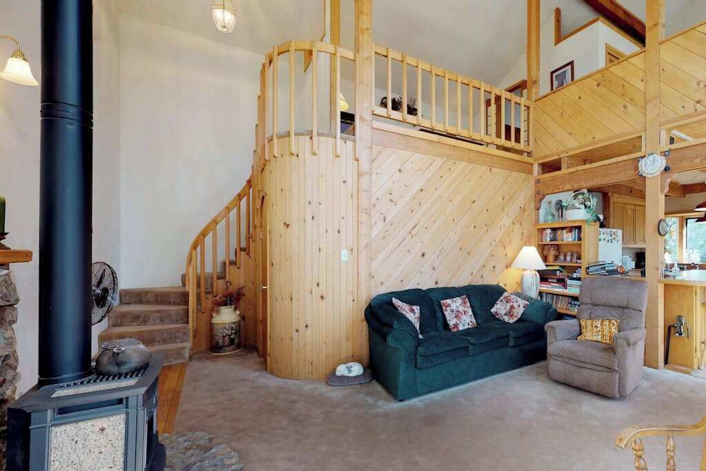 Un intérieur chaleureux avec un escalier en bois, un canapé vert, un fauteuil et une cheminée.