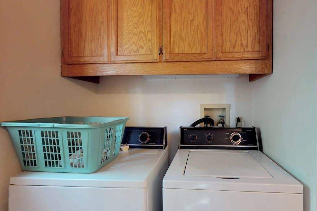 Een wasruimte met twee wasmachines en een houten kast erboven.