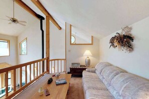 Ein Zimmer mit sichtbarem Holzbalken, einer Couch, einem Tisch mit Büchern und einer Lampe, sowie einem dekorativen Wandelement.