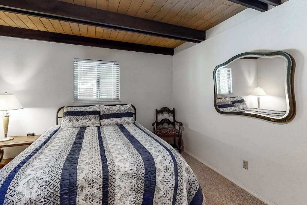 A bedroom with a bed, a chair, a lamp, a window, and a mirror.