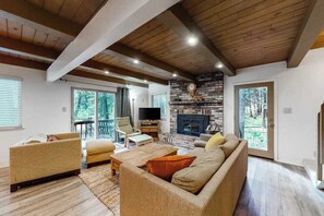 A spacious living room with a fireplace, comfortable seating, and a television. - Snowpeak Chalet - Big Trees Village (Camp Connell)