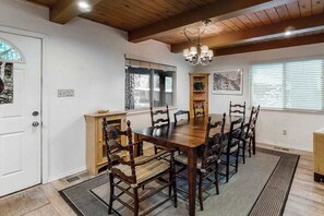 A dining room with a wooden table and chairs, a chandelier, and a view of the outdoors through a window. - Snowpeak Chalet - Big Trees Village (Camp Connell)