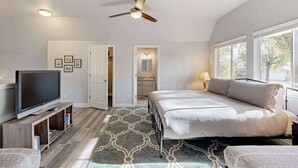 A bedroom with a bed, a television, a ceiling fan, and a view of the outside through large windows. - Serendipity - Pine Mountain Lake (Groveland)